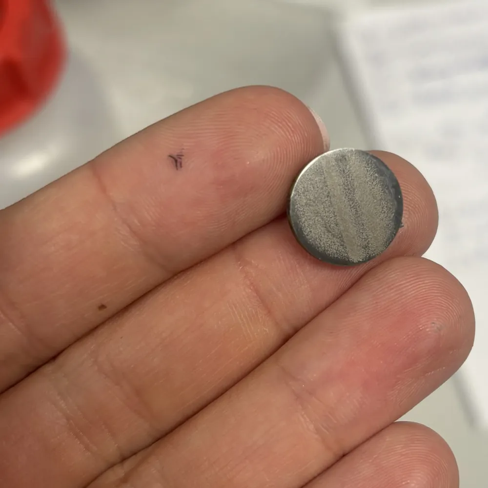 A small round test coupon held between two fingers