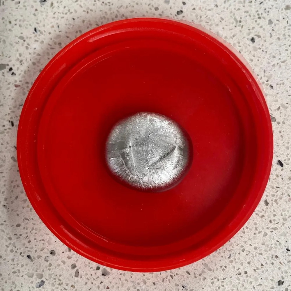 A cast alloy button with a crystalline surface, resting in a red lid